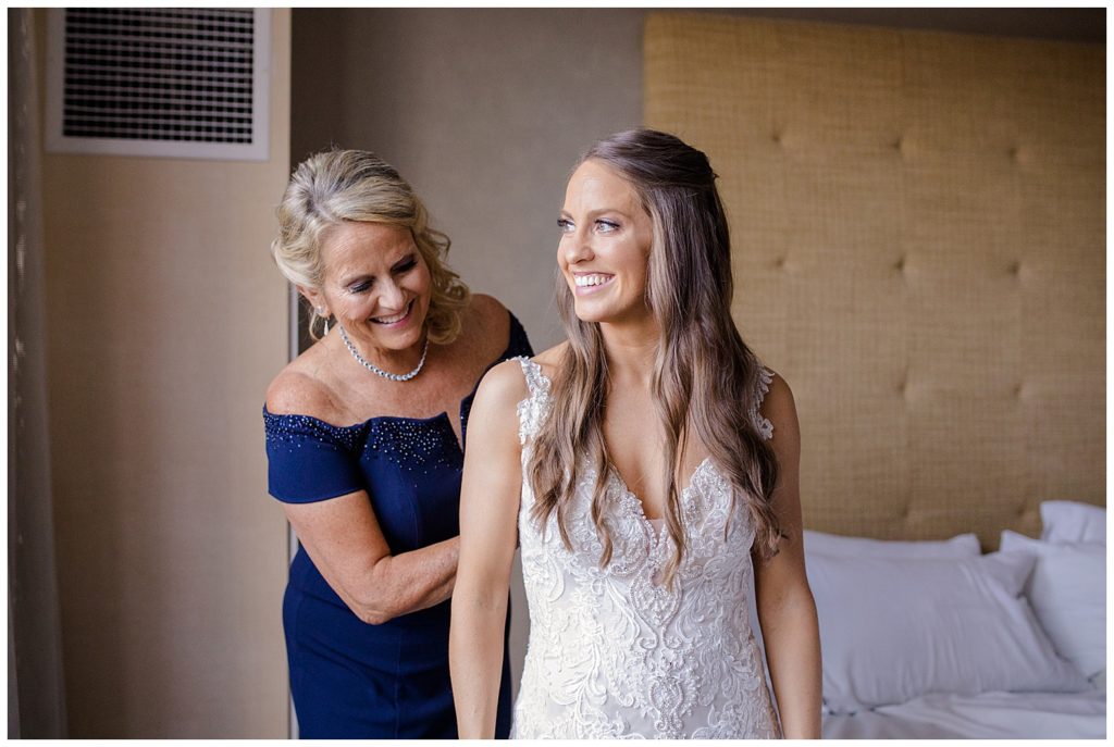 A picture of the bride smiling as her mother finishes zipping her wedding gown, getting ready for the wedding ceremony by Columbus wedding photographer, Alayna Parker Photography