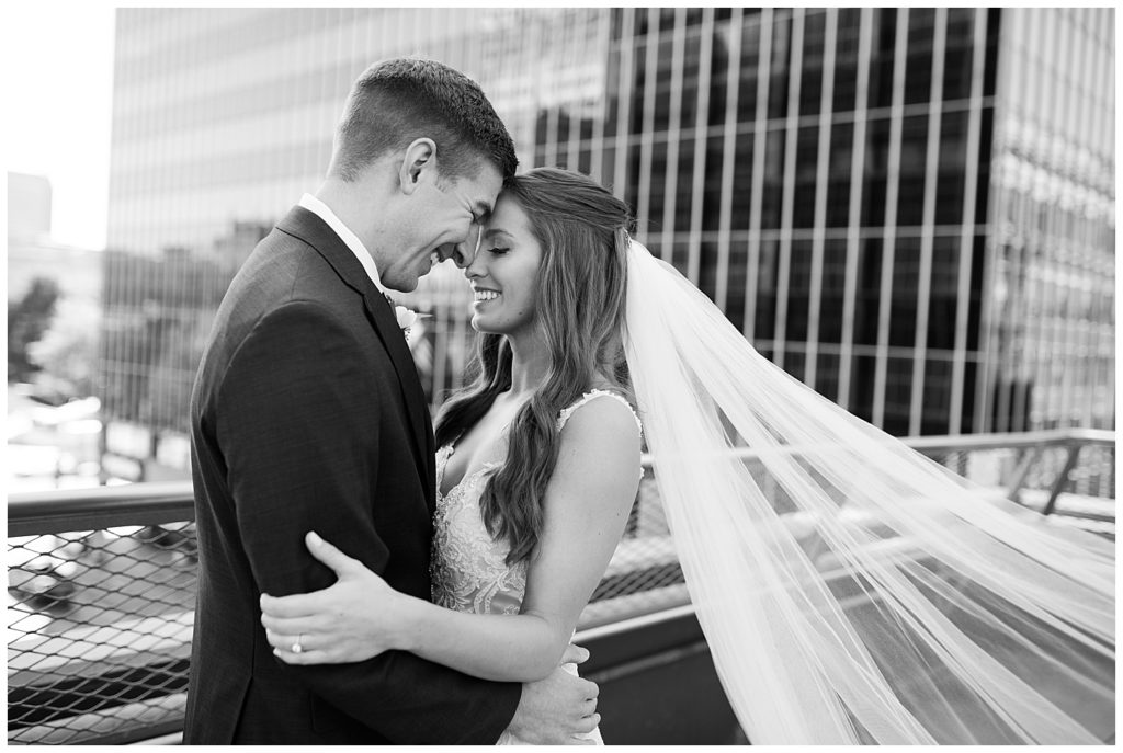 black and white image of bride and groom touching foreheads while veil blows in the wind on rooftop at renaissance hotel