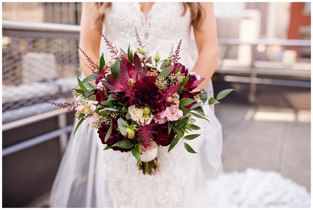 close up of bride holding bouquet of burgundy, pink, and white flowers and greenery
