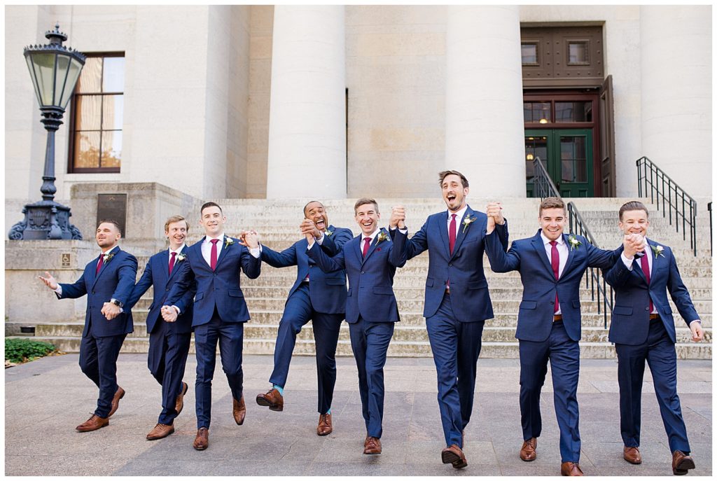 groom and groomsmen holding hands and skipping outside ohio statehouse