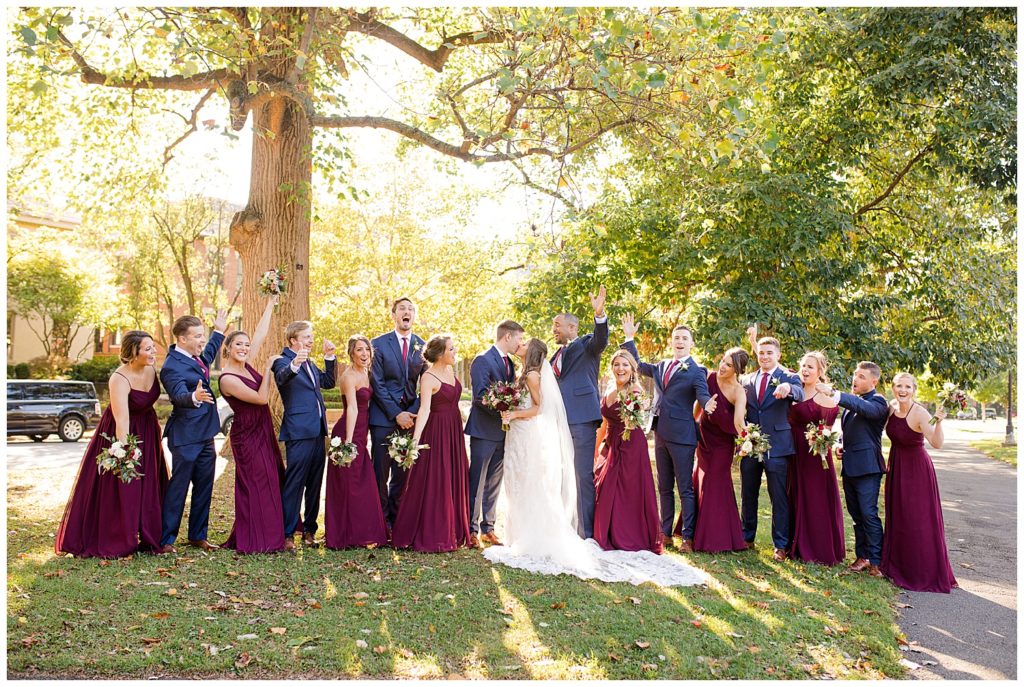 bride and groom kissing while bridal party cheers at schiller park in german village