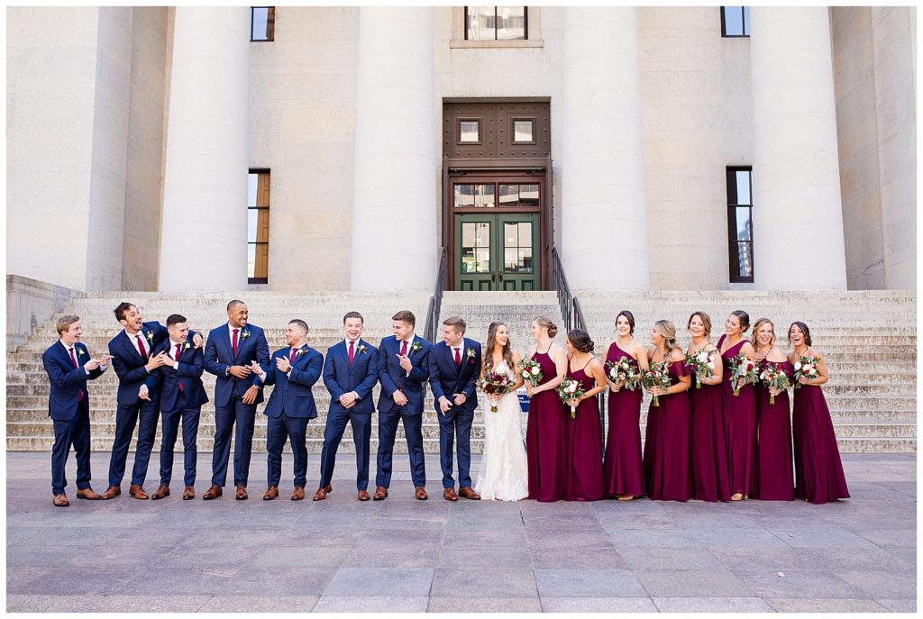 bride and groom and bridal party laughing and talking outside ohio statehouse