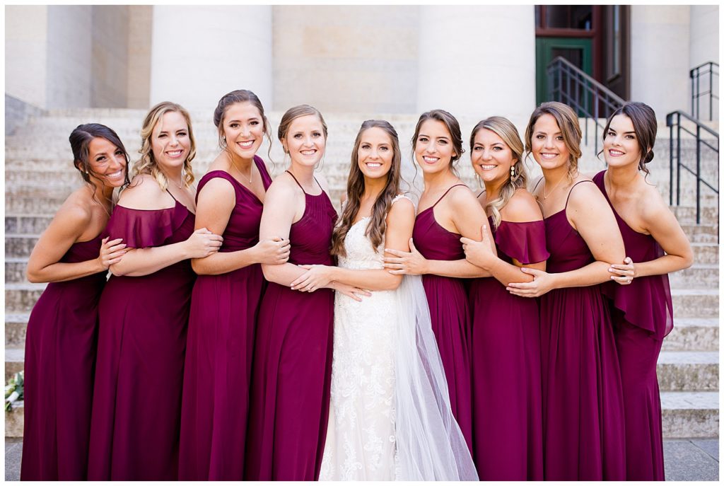 bride and bridesmaids holding on to each other and smiling at camera outside ohio statehouse