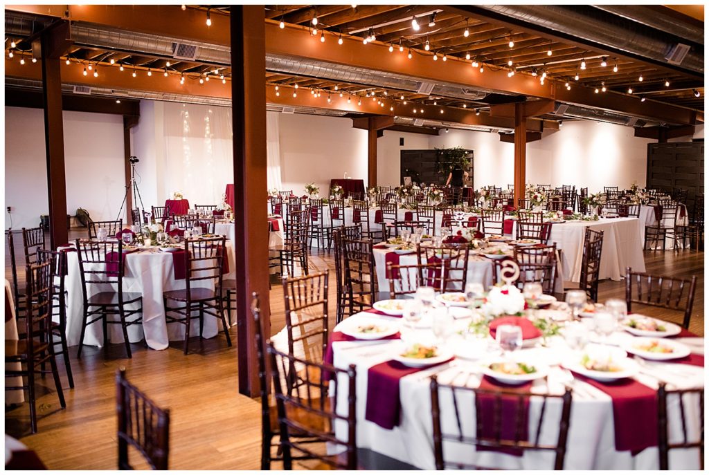 round tables with wooden chairs, white tablecloths, and burgundy cloth napkins at copius