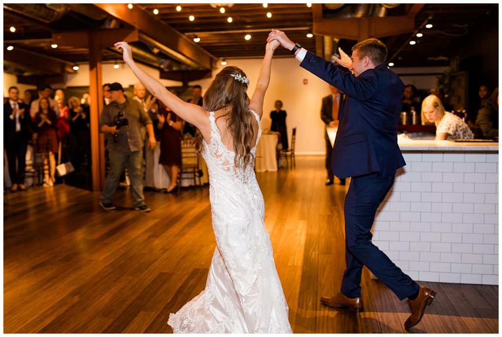 bride and groom throwing hands in air as they enter reception at copius