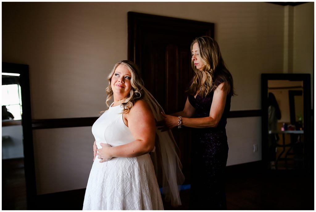 mother helping bride get dressed at the postmark