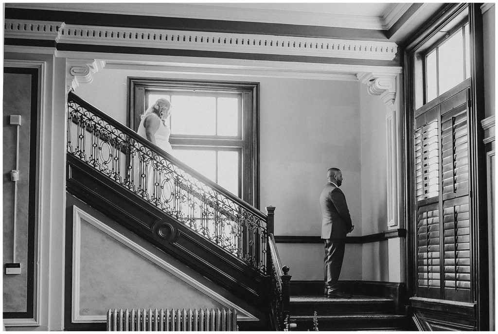 black and white image of bride walking down staircase to see groom at the postmark