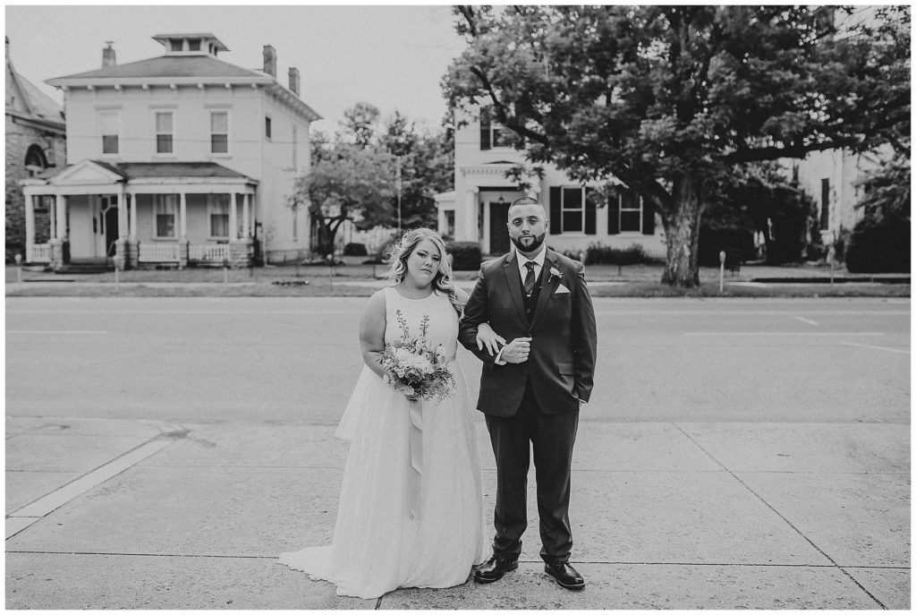 black and white image of bride and groom standing with arms links outside at the postmark