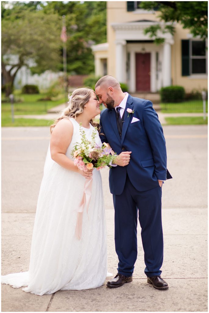 bride and groom smiling and touching foreheads outside at the postmark